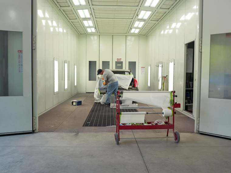 Technician masking a vehicle inside the downdraft paint booth at Jim Winter Collision